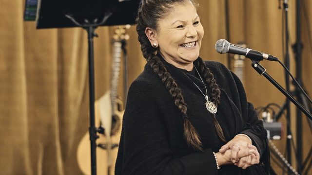 Rena Newell, Chief of Passamaquoddy Tribe at Sipayik, spoke at the event. Rena Newell, Chief of Passamaquoddy Tribe at Sipayik, wearing black sweater smiling standing at a microphone