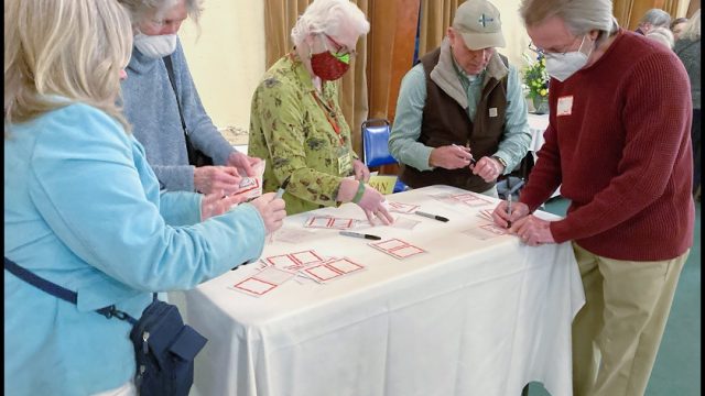 Members of the Wabanaki Alliance Coalition representing dozens of organizations and groups attended the Rising Voices event. Five people fill out nametags at a table.